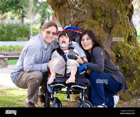 Happy Disabled Child In Wheelchair Surrounded By Parents Outdoors