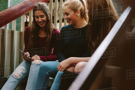 Three Young Women Sitting On The Steps And Looking At Mobile Phone