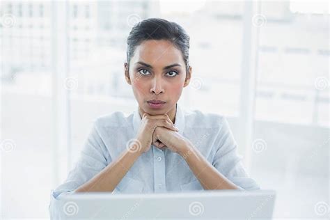Stern Businesswoman Sitting At Her Desk Looking At Camera Stock Photo