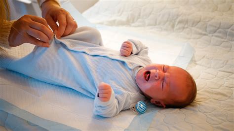 Little Newborn Baby Getting Dressed And Sucking Pacifier On Bed At