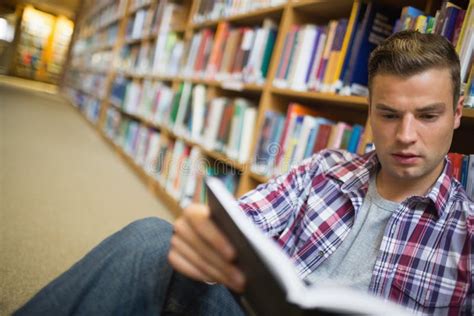 Serious Young Student Sitting On Library Floor Reading Book Stock Photo