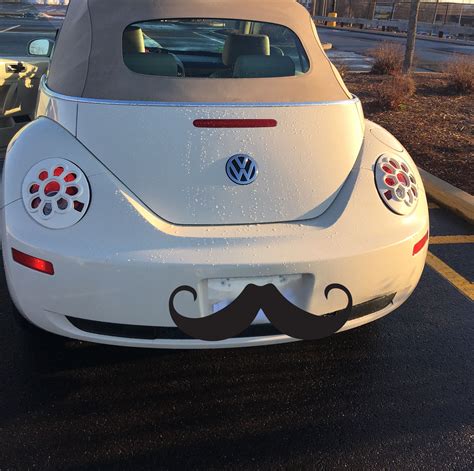 The Back End Of A White Car With A Mustache Painted On Its Side