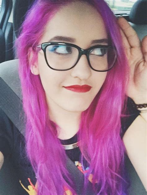 a woman with pink hair and glasses sitting in a car