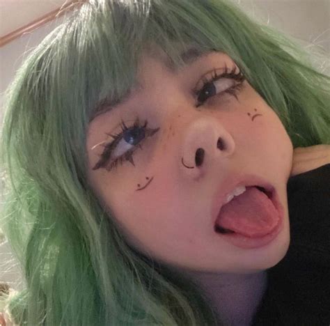 A Woman With Green Hair Has Fake Eyelashes On Her Face And Is Looking At The Camera