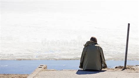 Lonely Woman Sitting By The Lake Watching The Melting Snow In Corona