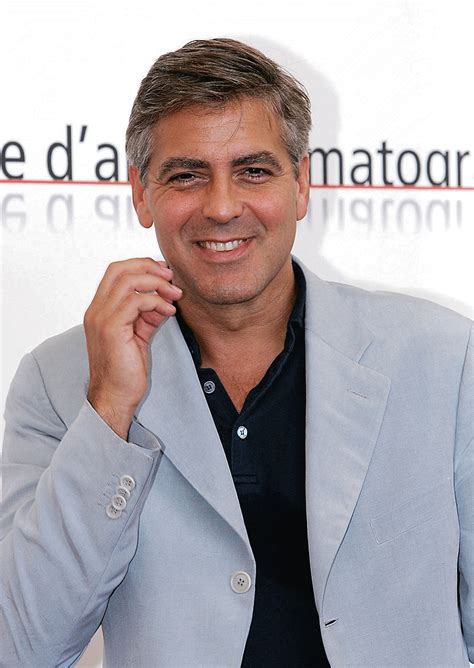 a man in a gray jacket smiles at the camera with his hand on his chin