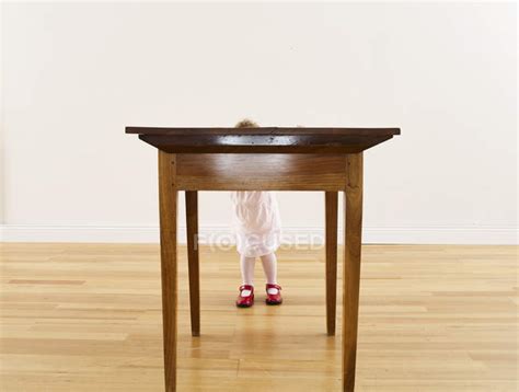 Little Girl Hiding Behind Wooden Table — Casual Front View Stock