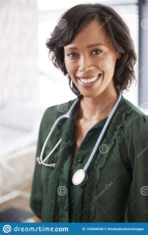 Retrato Del Doctor De Sexo Femenino Sonriente With Stethoscope Standing Por El Escritorio En