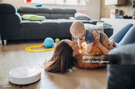 Young Mother Playing With Her Baby Boy While Robotic Vacuum Cleaner