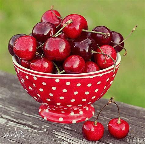 A Red Bowl Filled With Cherries On Top Of A Wooden Table