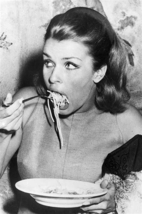 A Woman Is Eating Spaghetti From A Bowl While Sitting Down With Her Hands In Her Mouth