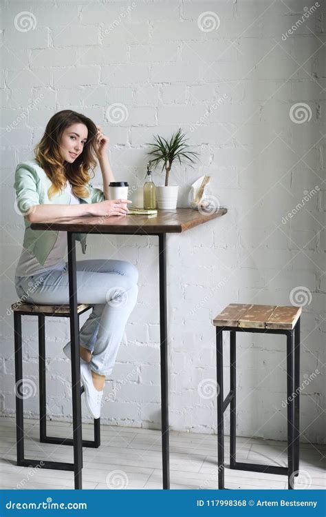 A Girl At A High Table Sits With Coffee Head Bent Over A White Brick