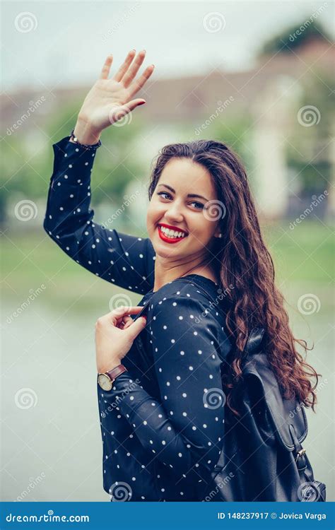 Portrait Of A Beautiful Young Woman Walking Outdoors Waving Her Hand