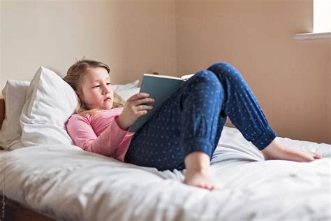 Girl Reading A Book While Lying On A Bed By Stocksy Contributor