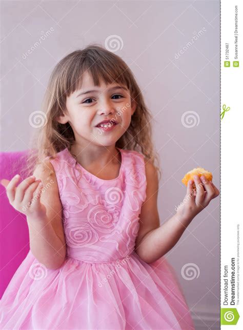 Маленькая девочка в розовом причудливом платье есть сладостное