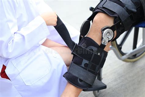 Physiotherapist Fixing Knee Braces Of Senior Man Leg With Sitting On