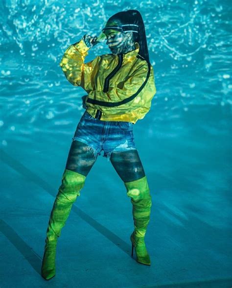 A Woman In Yellow Jacket And Blue Shorts Standing Under Water With Her Arms Behind Her Head