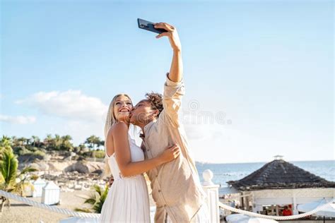 Happy Couple In Love Kissing Taking Selfie Together With Smartphone On The Beach Honeymoon