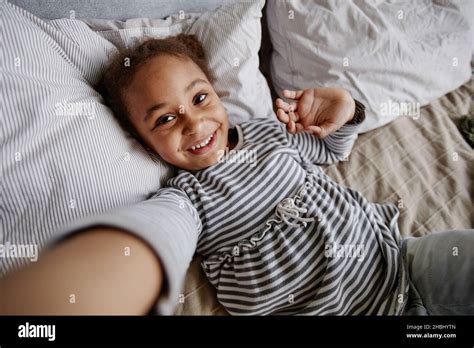 High Angle Portrait Of Cute African American Girl Taking Selfie Photo While Lying On Bed Stock