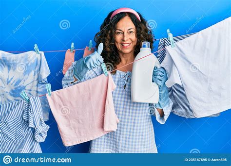 Middle Age Hispanic Woman Doing Laundry Holding Detergent Bottle