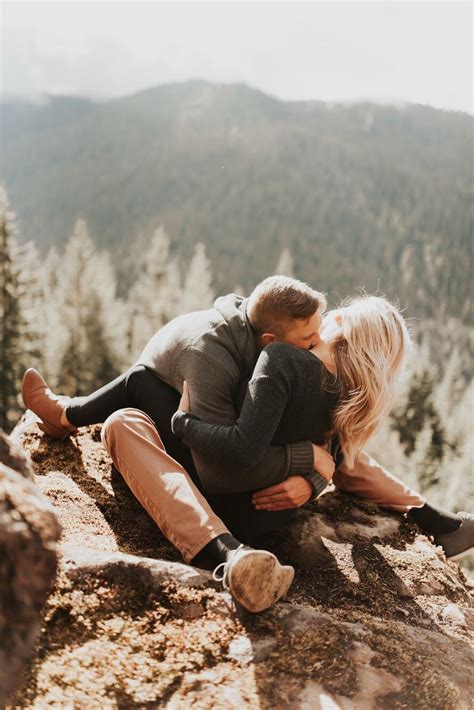 A Man And Woman Sitting On Top Of A Mountain Hugging Each Other With