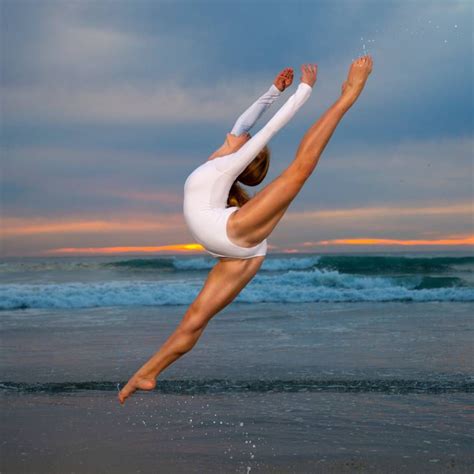 A Woman In White Is Doing A Handstand On The Beach At Sunset Or Sunrise