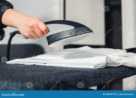 Woman Using Steaming Iron To Ironing Fashion Shirt In Laundry Room