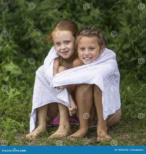 twee ongehoorzame meisjes die op het strand in een handdoek na zitten baden in het meer de zomer