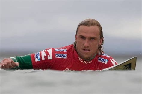 a man laying on top of a surfboard in the ocean while wearing a red and green shirt