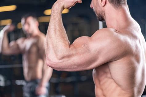 Close Up Of Muscular Young Man Posing With Biceps Contraction Reflection In The Mirror Stock