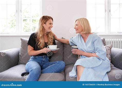 Senior Mother With Adult Daughter Sitting On Sofa Indoors Drinking
