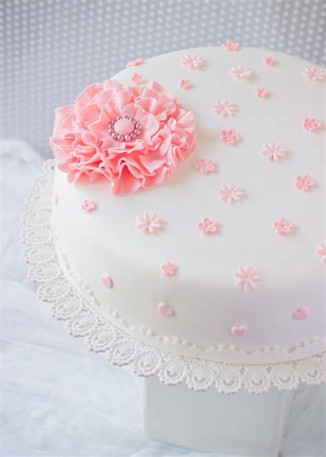 A White Cake With Pink Frosting And A Flower On Top Sitting On A Lace