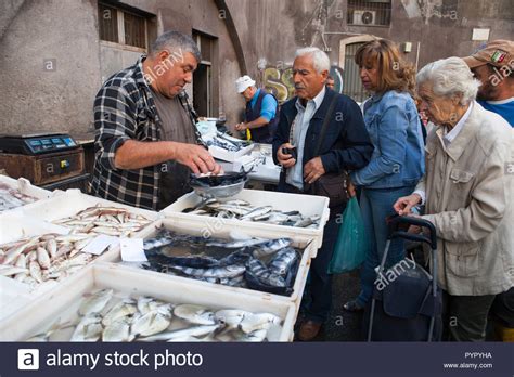 A Fishmonger Serves Customers In The Fish Market In Catania Sicily