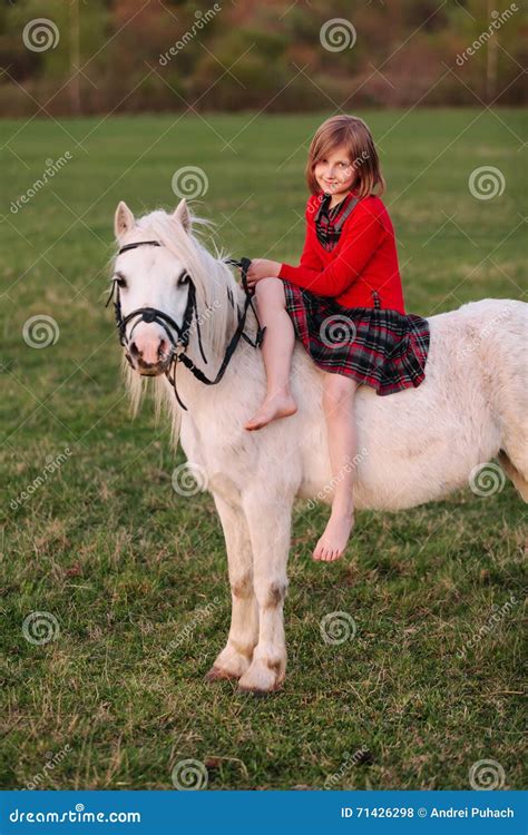 Little Young Girl In Dress Sitting On A Pony Riding Lady Stock Photo