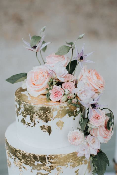 A White And Gold Wedding Cake With Pink Flowers On The Top Surrounded