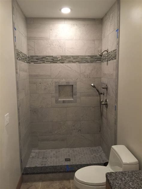 This stone tile bathroom design by mwai architects makes use of geometry and pattern in a small space to add character and visual interest. 12x24 grey wall tiles, shower niche, 2x2 mosaic floor ...