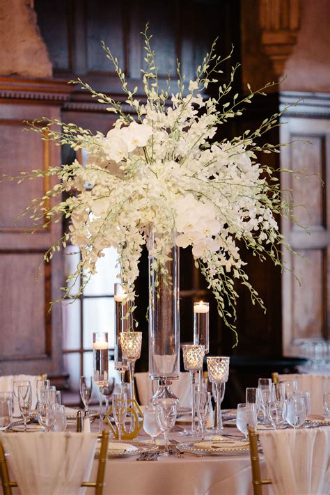 a tall vase filled with white flowers sitting on top of a table covered in glasses