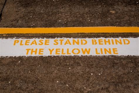 Image Of Warning Sign To Please Stand Behind The Yellow Line At