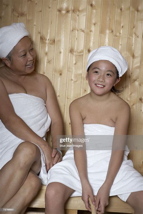 Grandmother And Granddaughter Wrapped In Towels Smile As They Enjoy A Hot Sauna At The Spa High