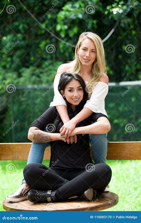 A Pair Of Proud Lesbian In Outdoors Sitting On A Wooden Table Blonde Woman Is Hugging A