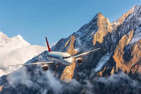 Airplane Is Flying Over Low Clouds Against Mountains Stock Photo