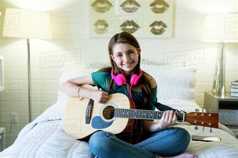 Portrait Of Happy Teenage Girl Playing Guitar In Bedroom Stock Photo