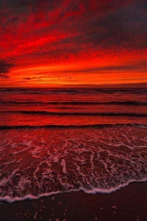 An Orange And Red Sunset Over The Ocean With Waves Coming In To Shore