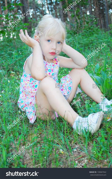 In The Summer Bright Sunny Day In Forest A Little Serious Girl Is Sitting In The Tall Grass