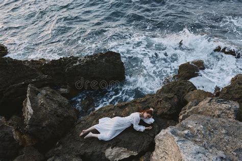 Barefoot Woman In Long White Dress Wet Hair Lying On A Rocky Cliff