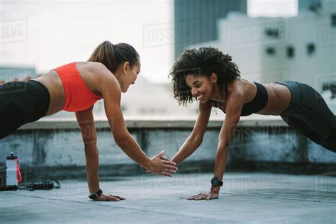 two fitness women doing push ups with one hand while touching their other hand cheerful women