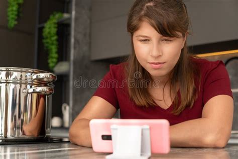 Woman Watching Video On Mobile Phone In Kitchen Counter Stock Photo