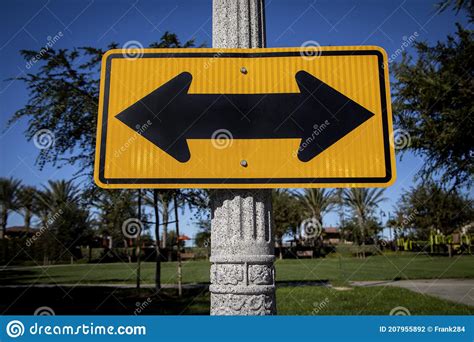 Yellow Road Sign On A Street Pole With Arrows Pointed In Opposite