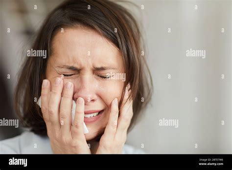 Close Up Portrait Of Disheveled Adult Woman Crying Hysterically With Eyes Closed And Holding