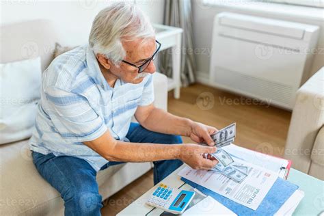 Old Retiree Man Sit On Couch Holding Receipt Paper Calculates On